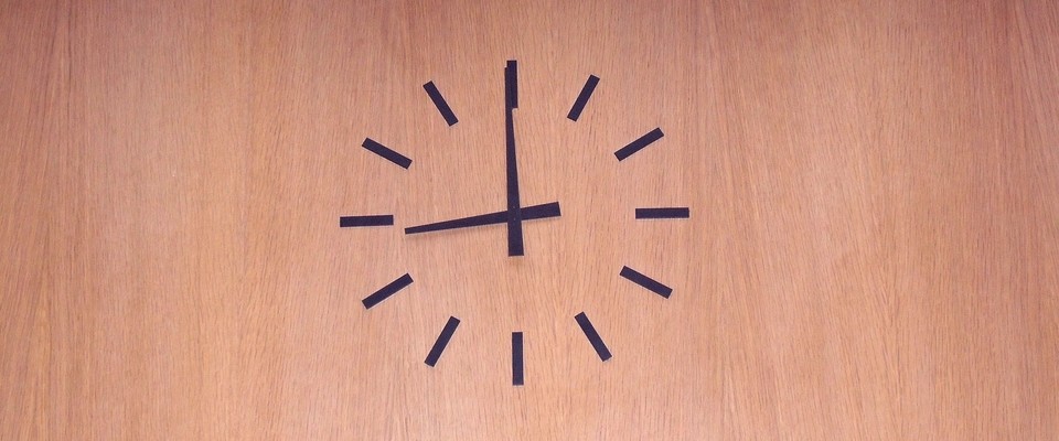 Zu sehen ist eine Uhr auf einer braunen Wand, sie zeigt 09:00 Uhr an.